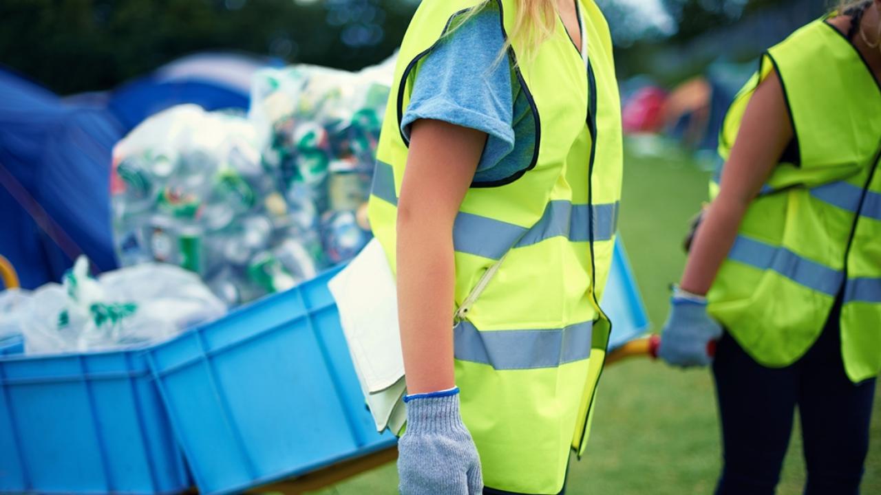 two people wearing reflective vests carrying carts full of recycling