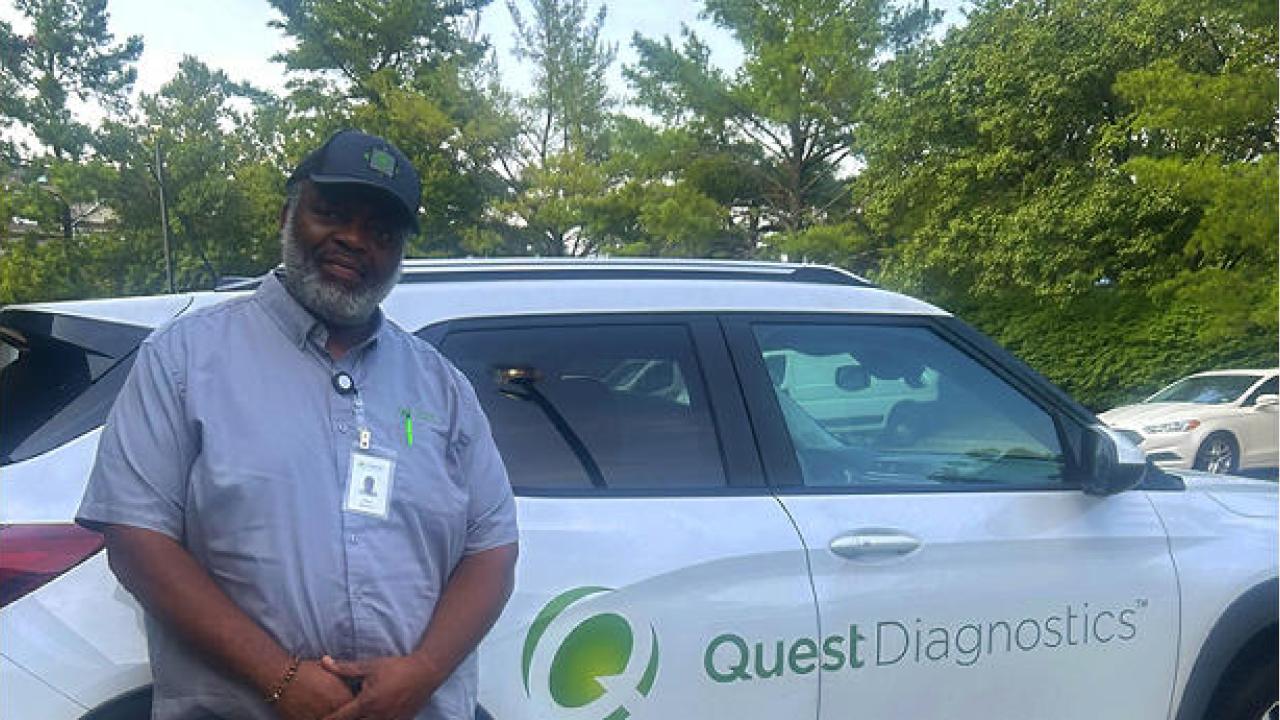 A person leaning against a white car that has the Quest Diagnostics logo on the side