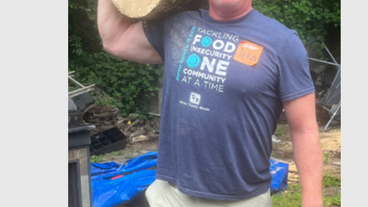 John Fittro holding a large log on one shoulder.
