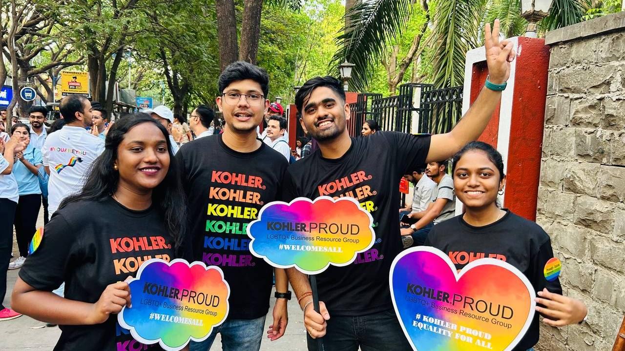 A group posed outside holding rainbow colored, shaped boards "Kohler Proud"