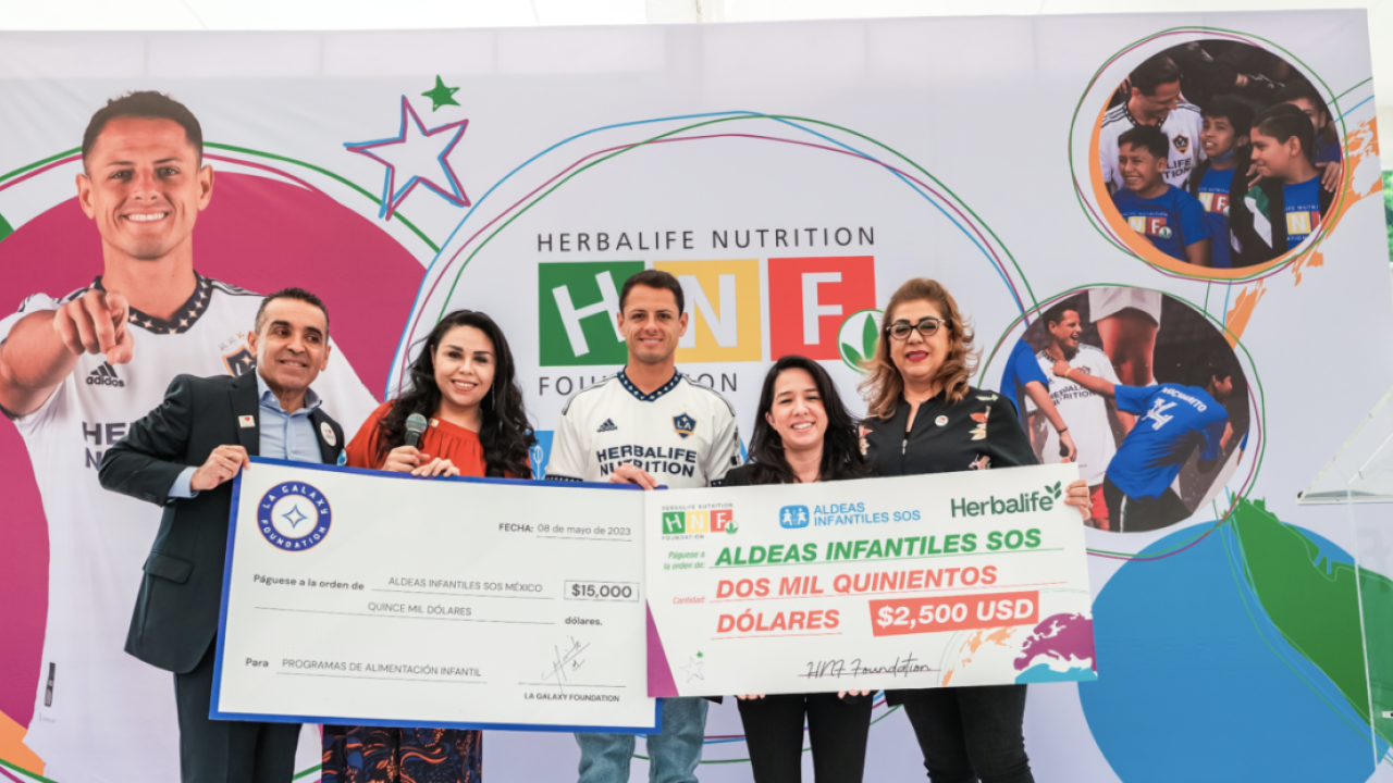Five people in front of a large banner, holding up two checks.