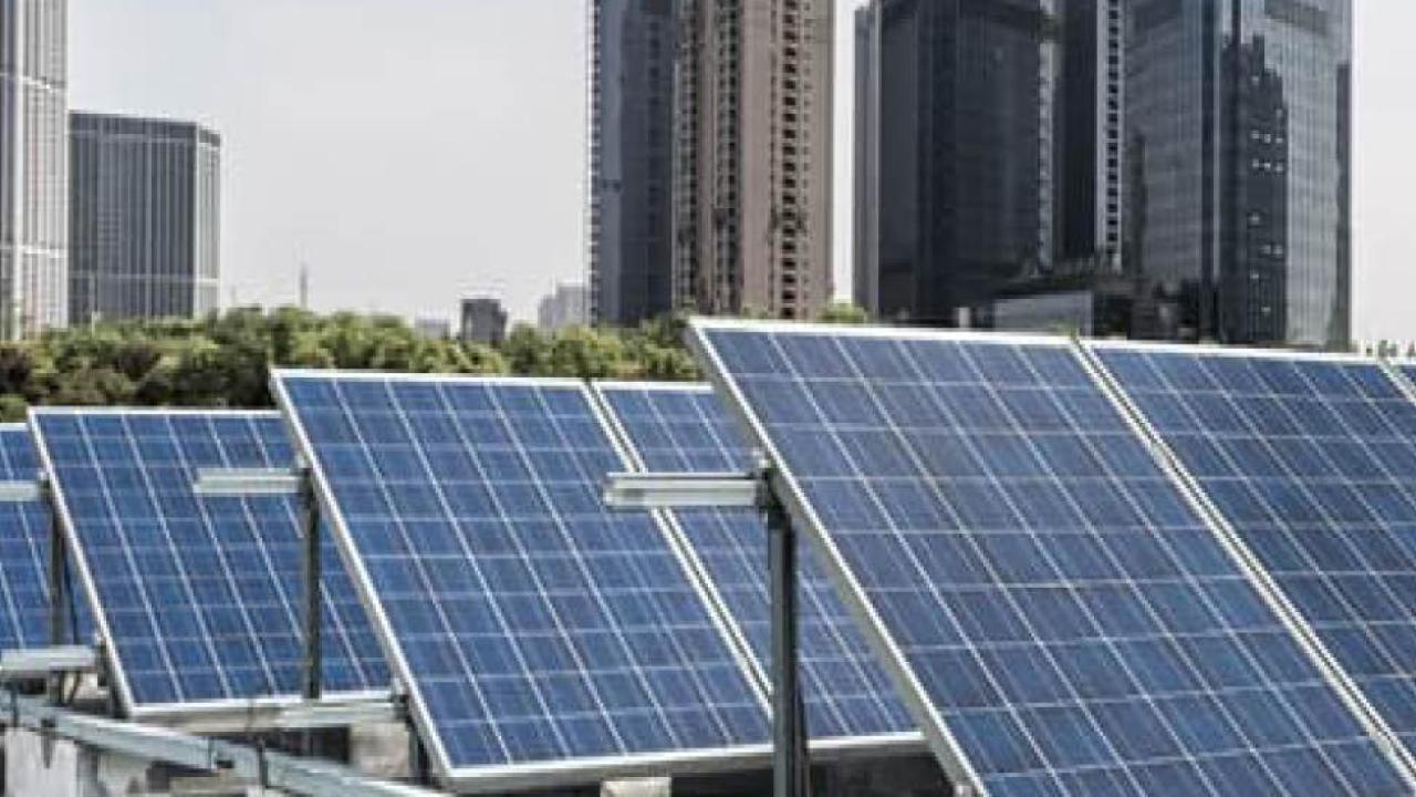A row of tilted solar panels, a city-scape behind them