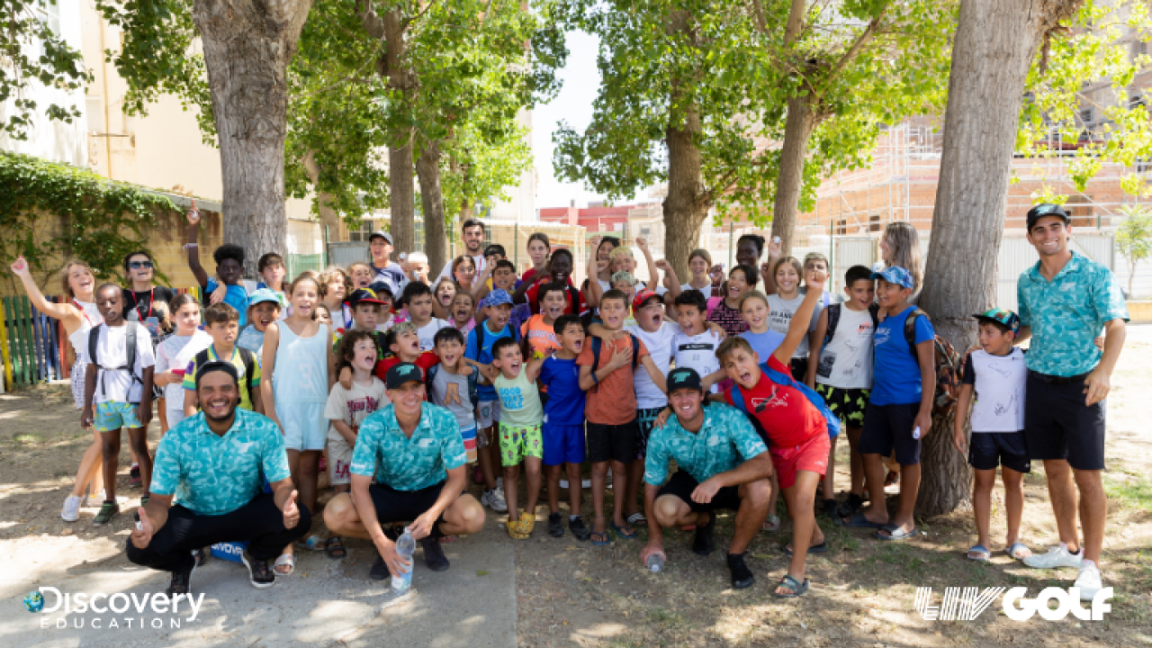 A large group photo of children and adults, taken outside underneath trees 