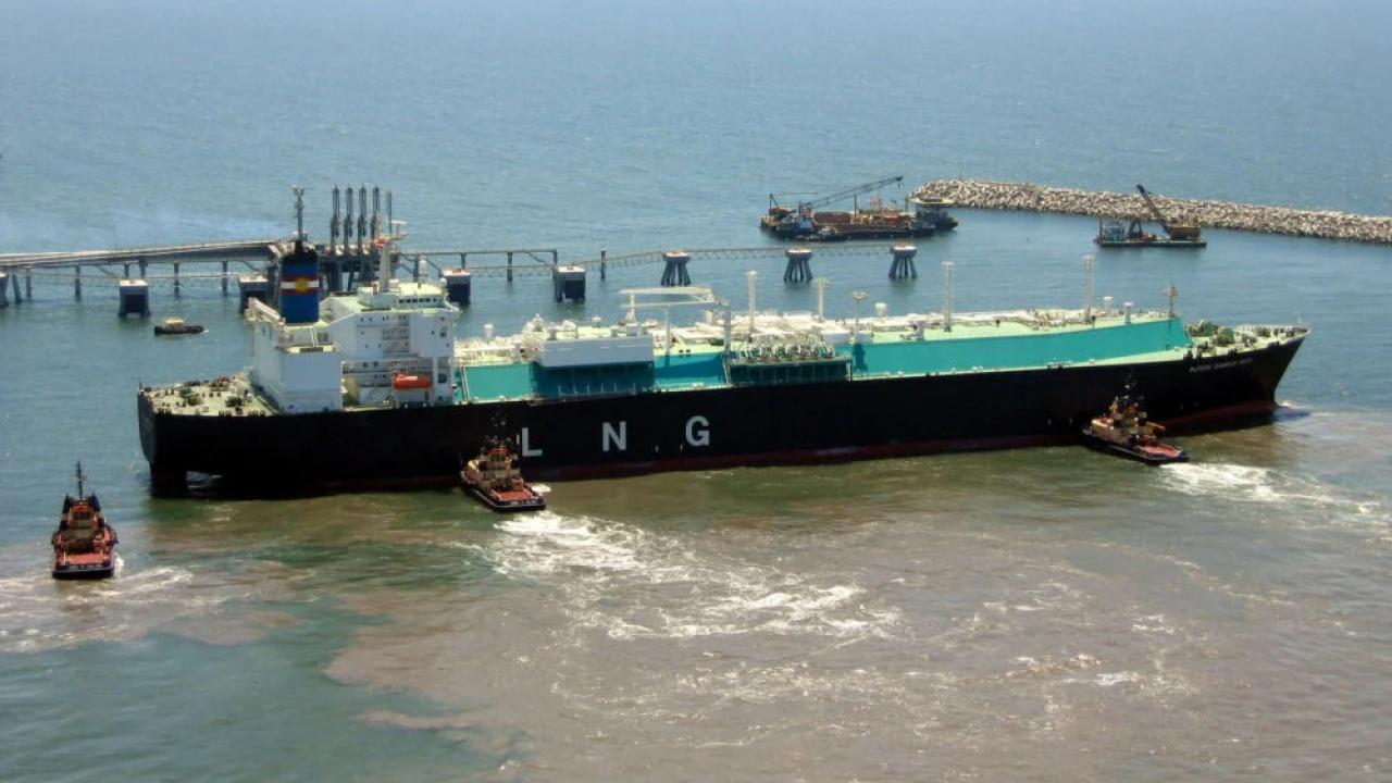 A large tanker with "LNG" on the side being pushed by smaller boats