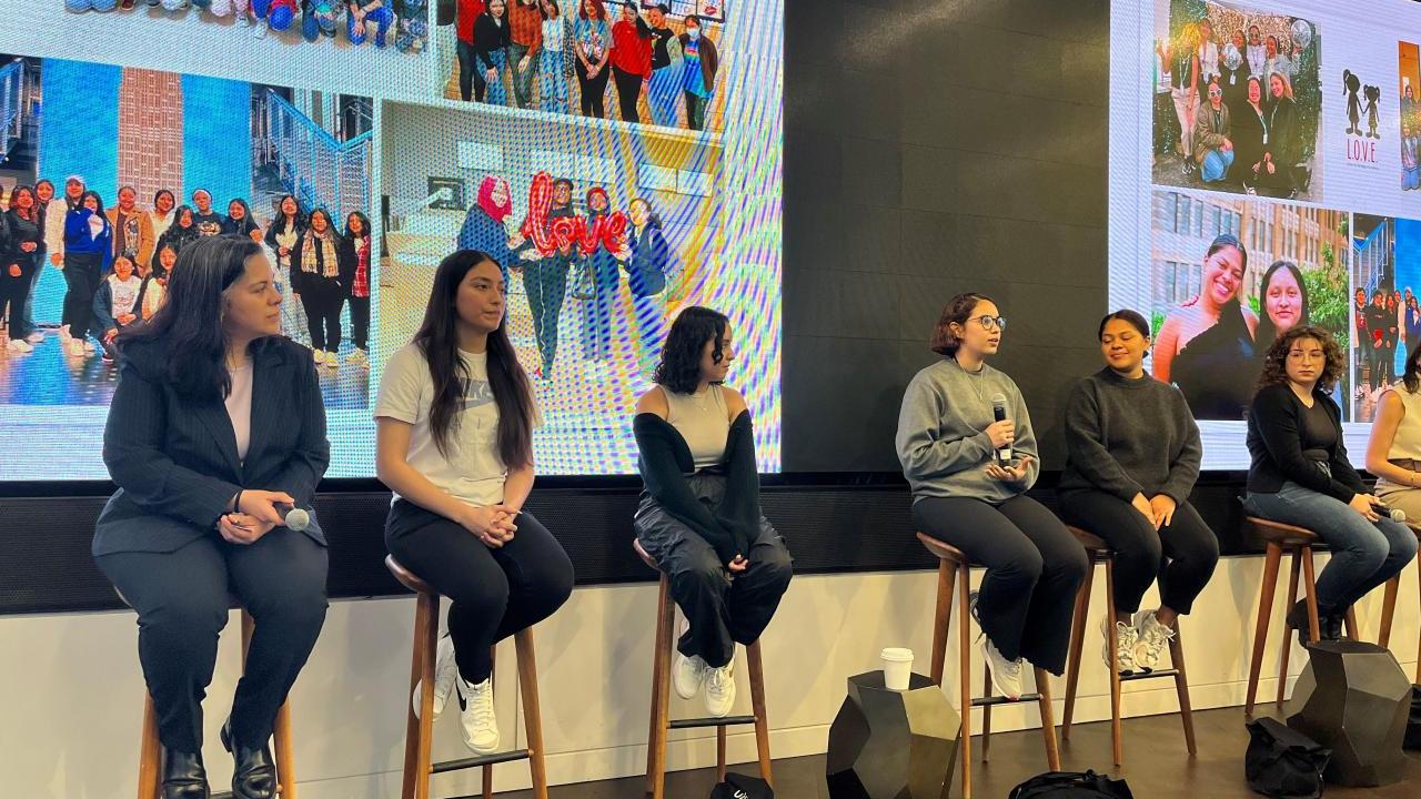 Six women sitting on stools engaged in a panel discussion