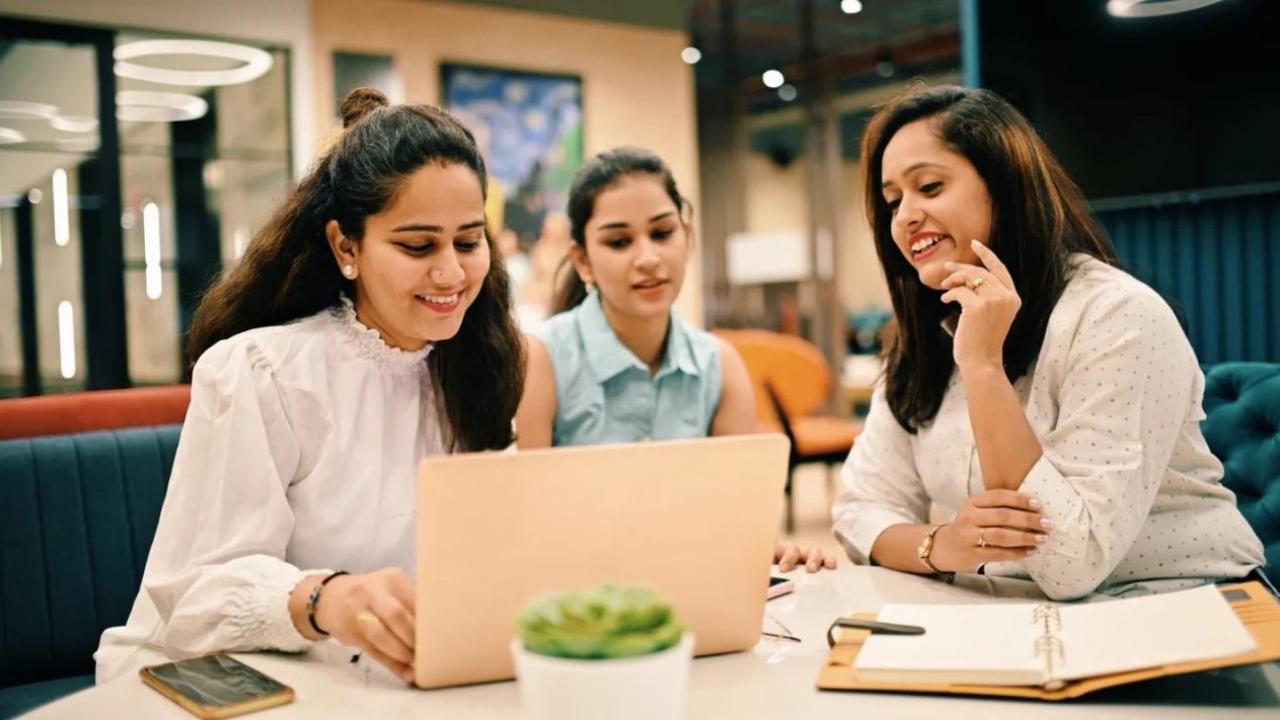 Three people sat at a table looking at a laptop