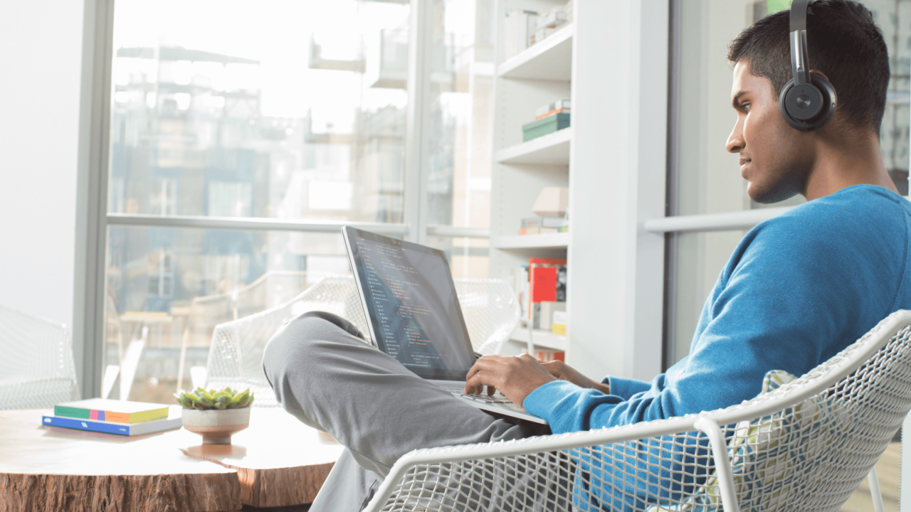 Person wearing headphones, sat on a chair with a laptop on their lap