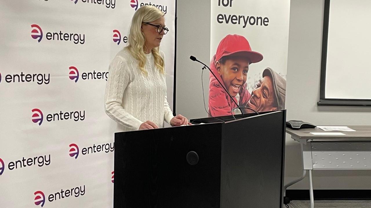 A person stood at a microphone stand, in front of an Entergy backdrop 