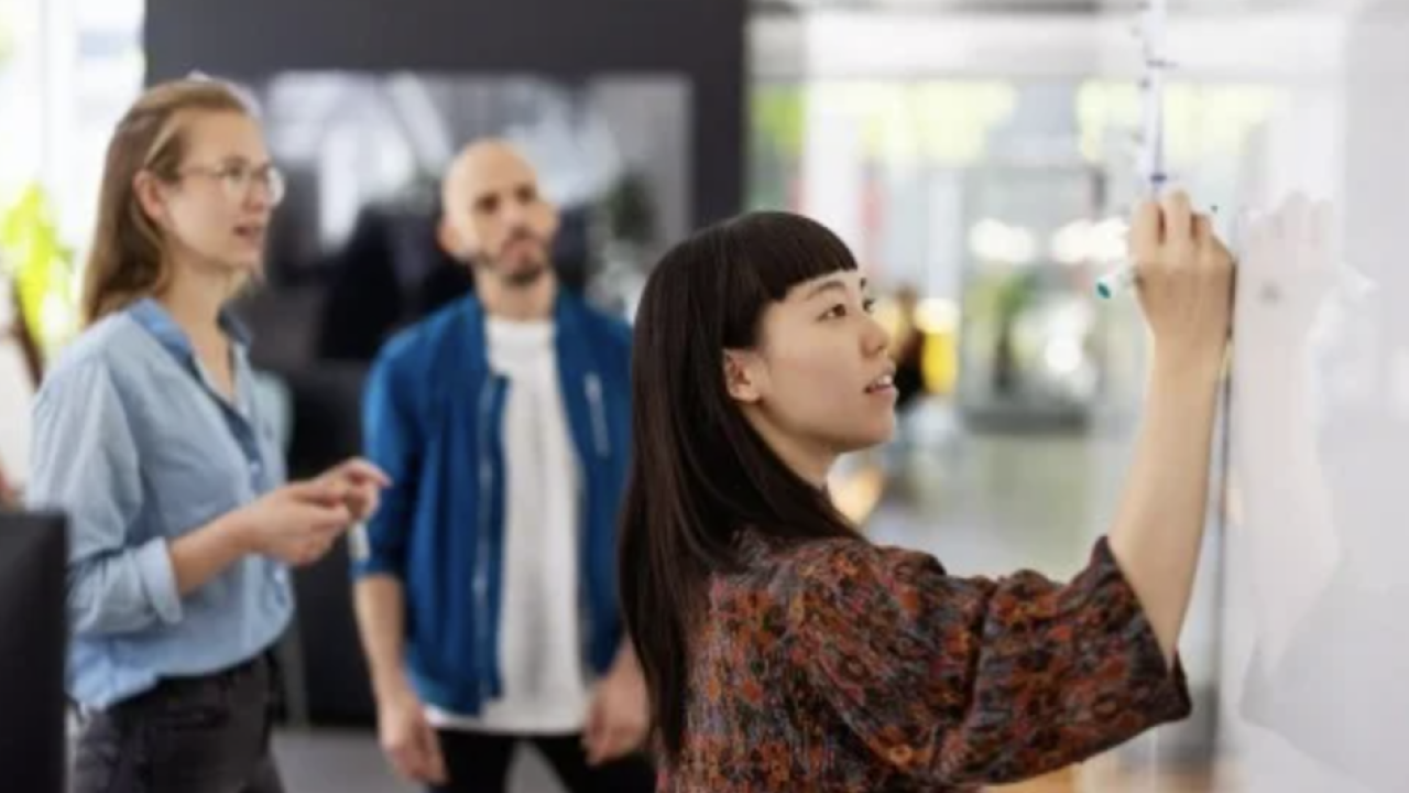 A woman making a presentation on a white board for two other people.