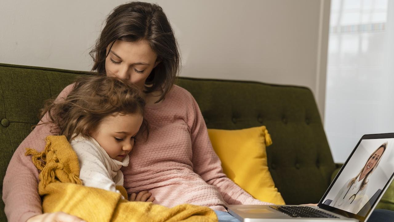 Mom and daughter seated on a couch together.