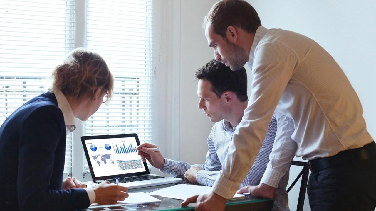 Three coworkers gathered around a computer displaying data visualizations