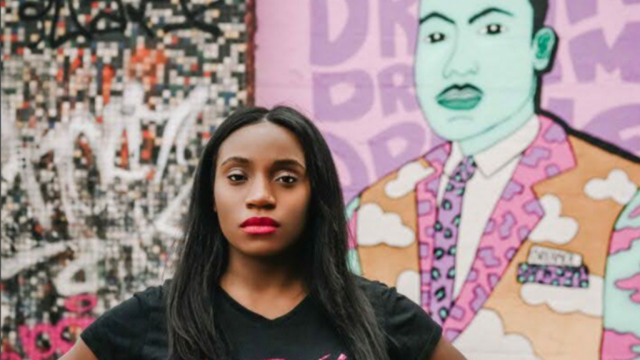 Courtney Wright wearing a "LipRevolt" tshirt in front of a mural of Martin Luther King