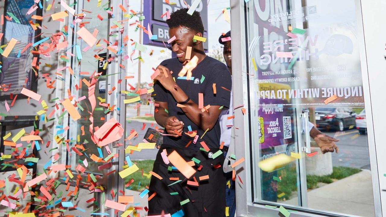smiling person walking into a taco bell through confetti