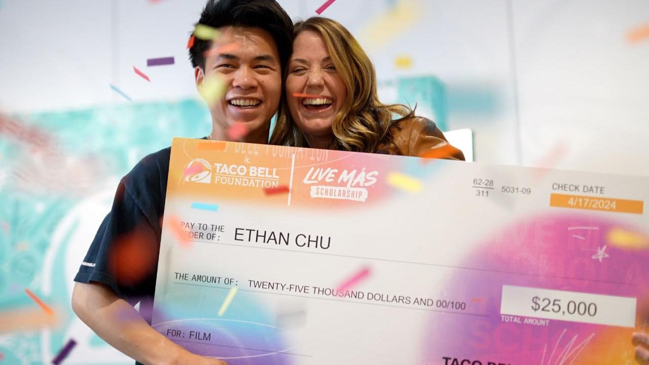 Two smiling people posed with a large check. Confetti falling around them.