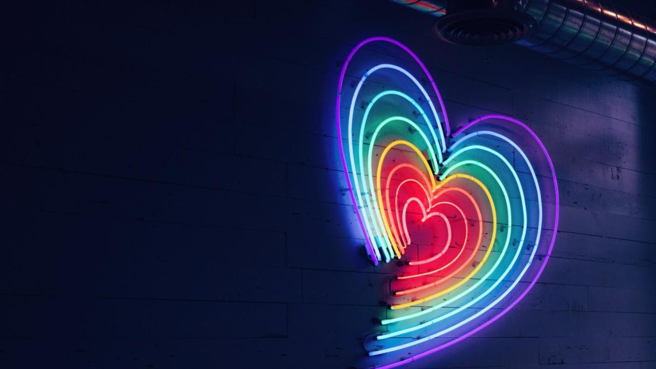 A rainbow heart in neon lights on a dark wall.