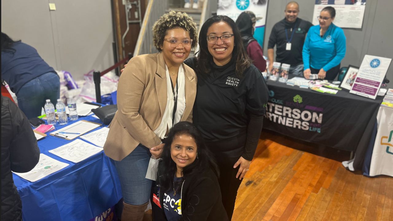 Three people pose for the camera in front of tables set up for different organizations.