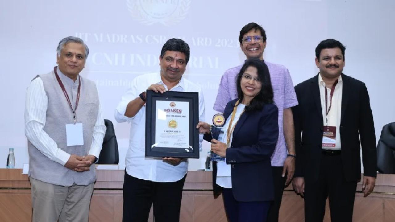 Five smiling people posed, two holding a plaque.