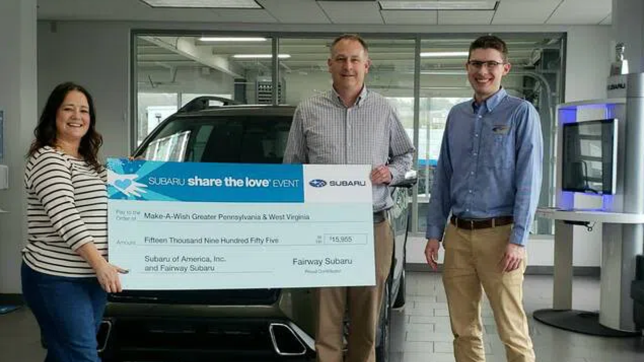 Three people holding donation check in front of car in showroom