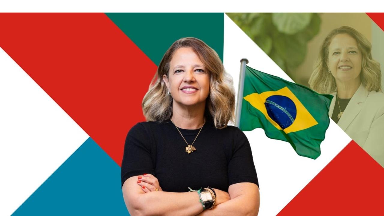 A person stood with their arms folded in front of a flag of Brazil