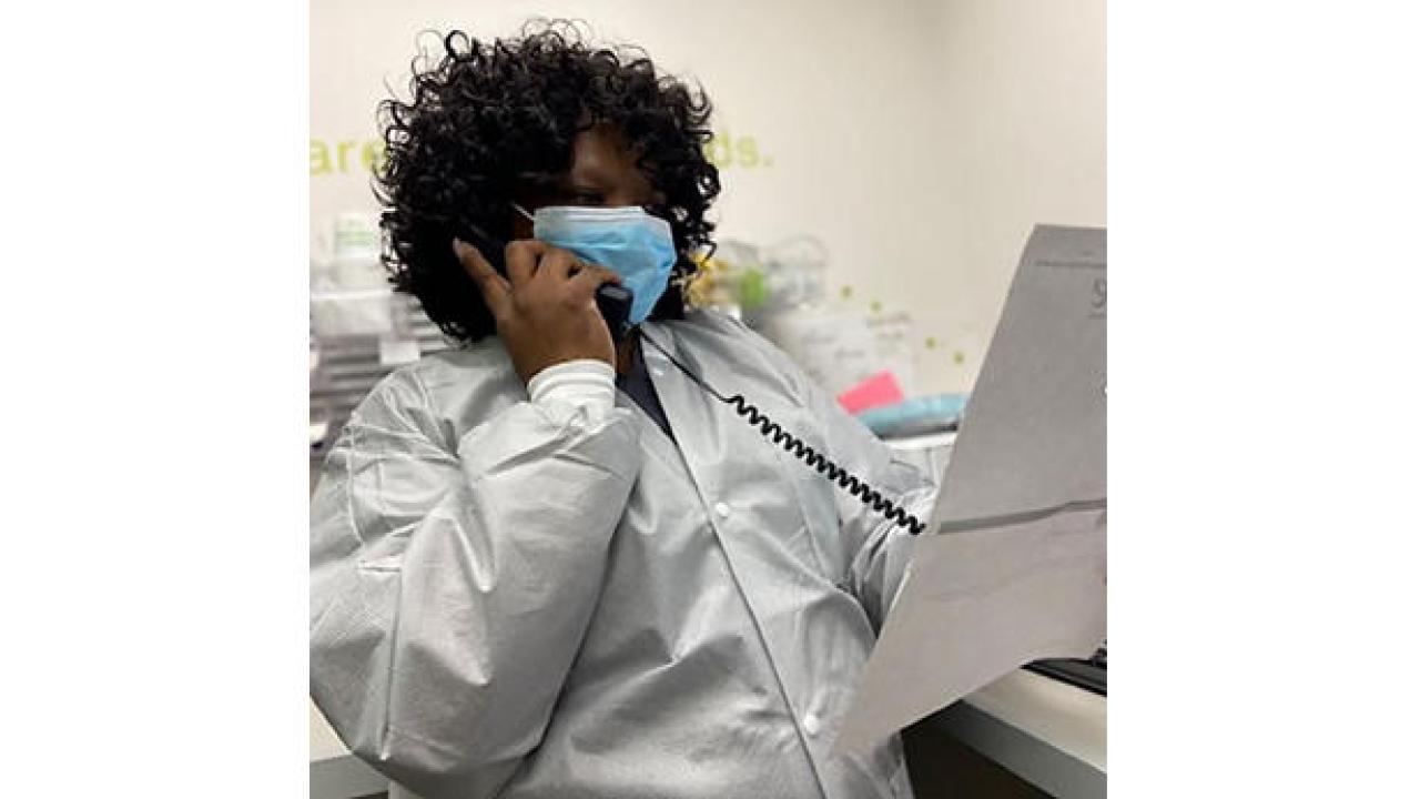 Marissa McGhee wearing a face mask, using a telephone while looking at a piece of paper