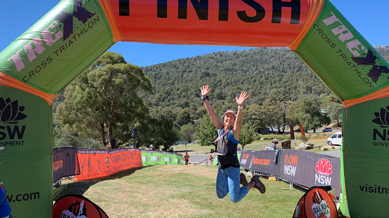 Melinda Toraya jumping with arms in the air under the finish line for the trex cross triathlon