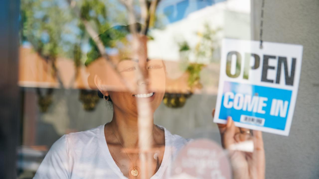 Woman in a glass window putting up an Open, Come in sign.