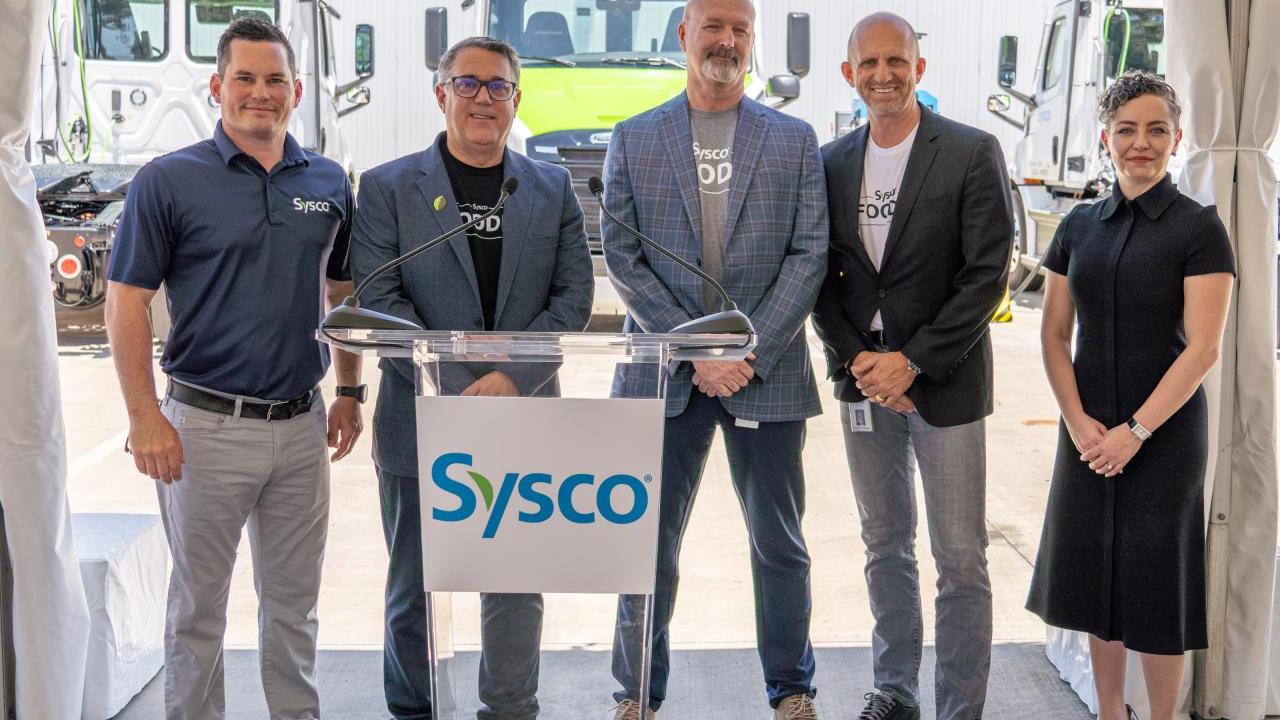 Five Sysco staffers standing in front of electric trucks. 