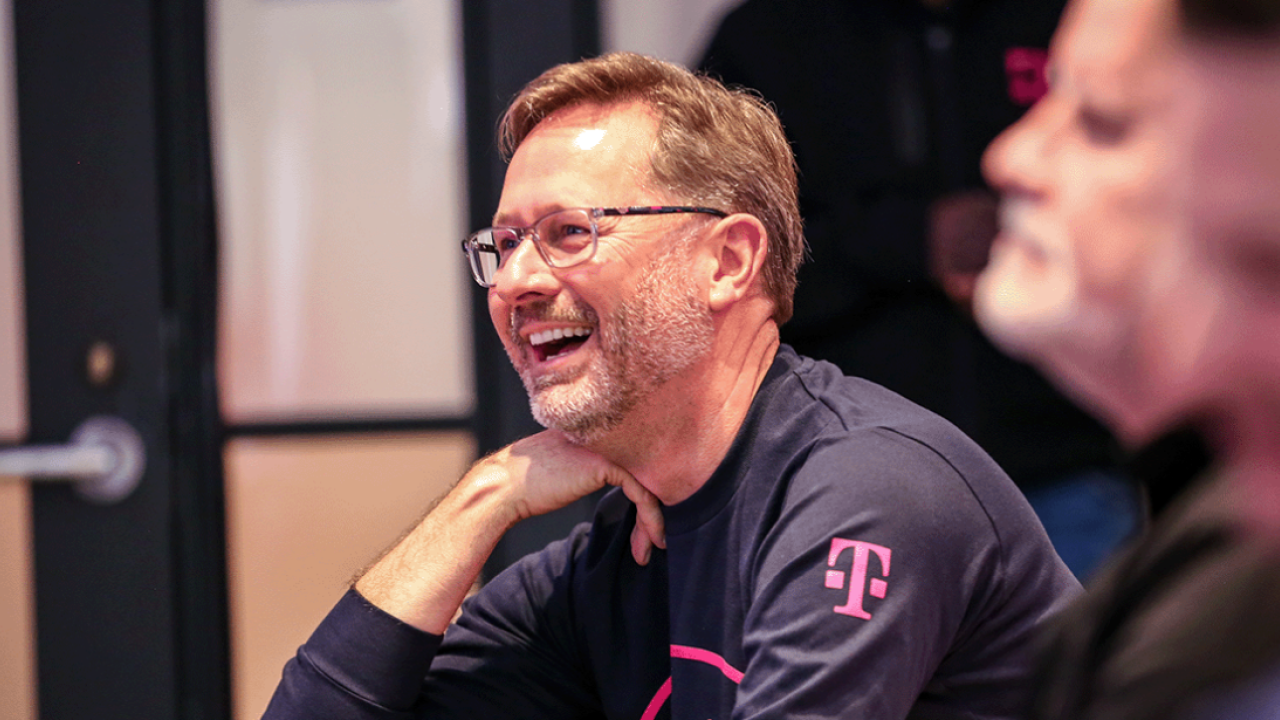 Mike Sievert smiling, right hand under their chin. Others to the left of them.