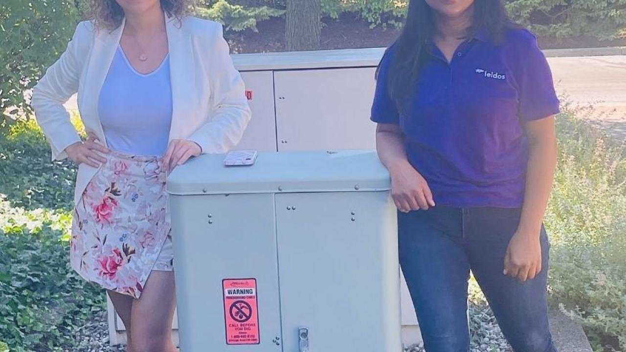 Two people posed next to an outdoor electrical box.