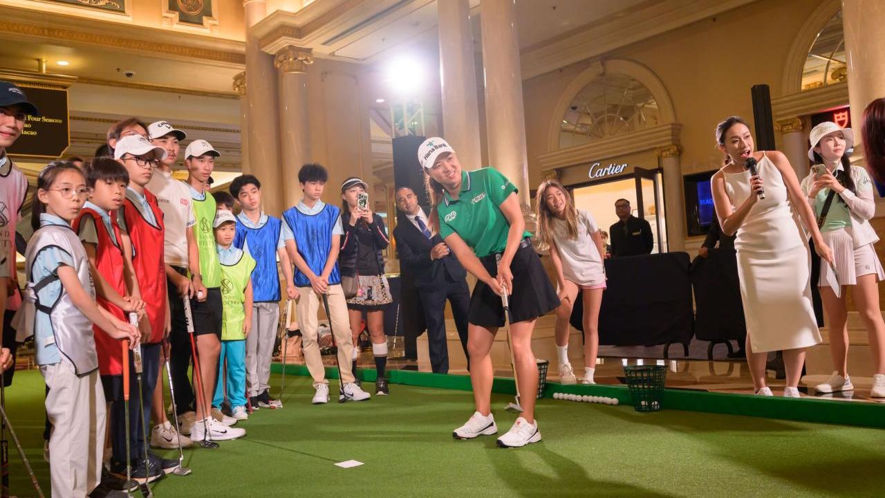Professional golfer putting on an indoor green as others look on.