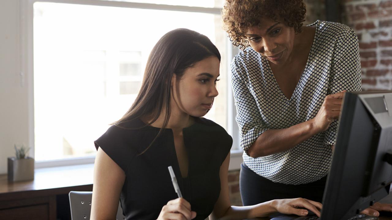 Older woman stands behind young woman on the computer