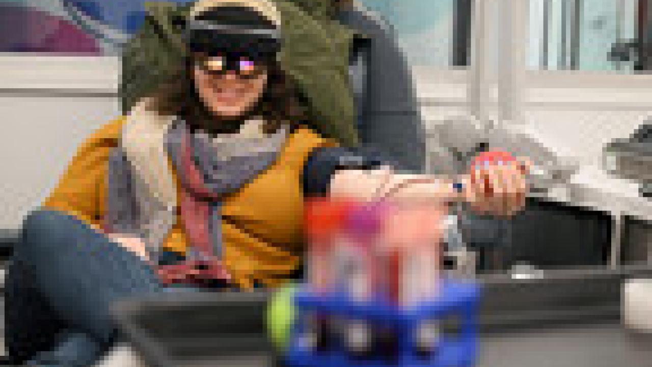 A person reclined and donating blood. They are wearing a VR headset and smiling.