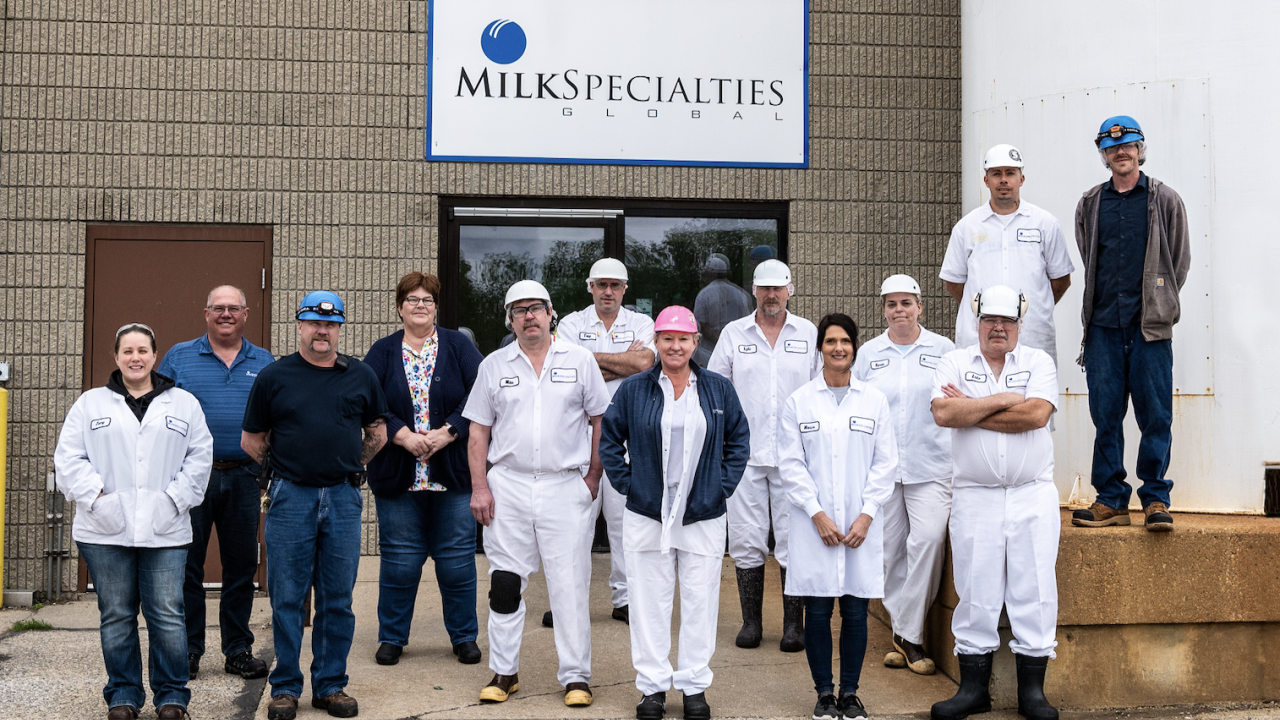 A small group of people posed outside a building. Some in all-white uniforms. "Milk Specialties" sign behind them. 