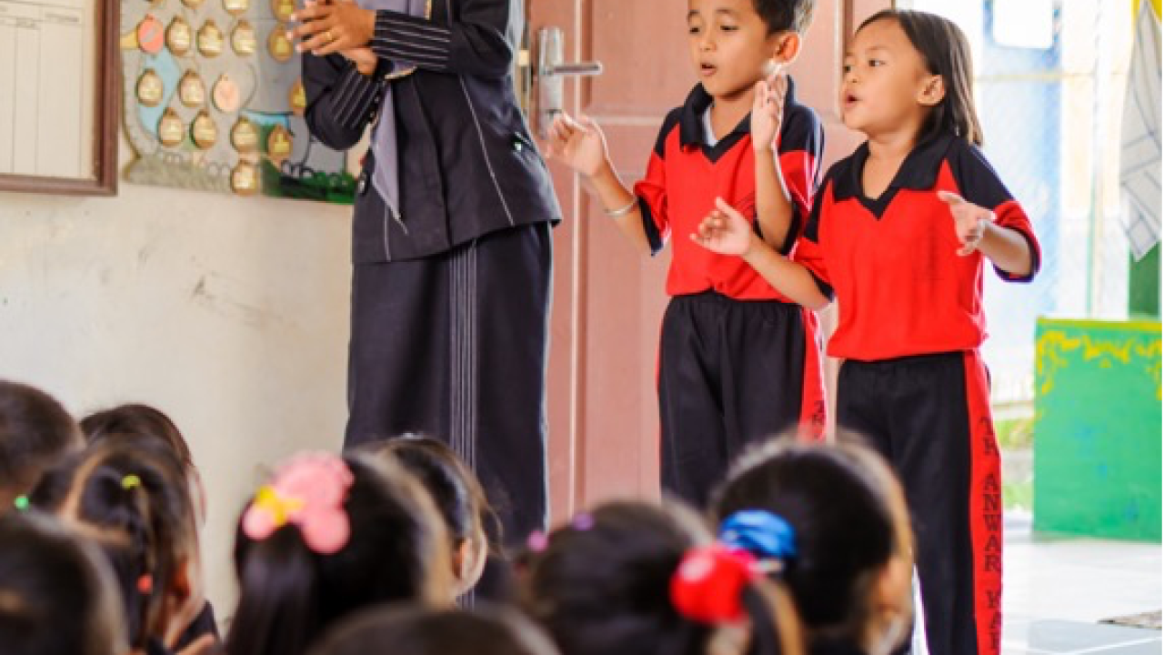 teacher and two students standing in front of sitting class
