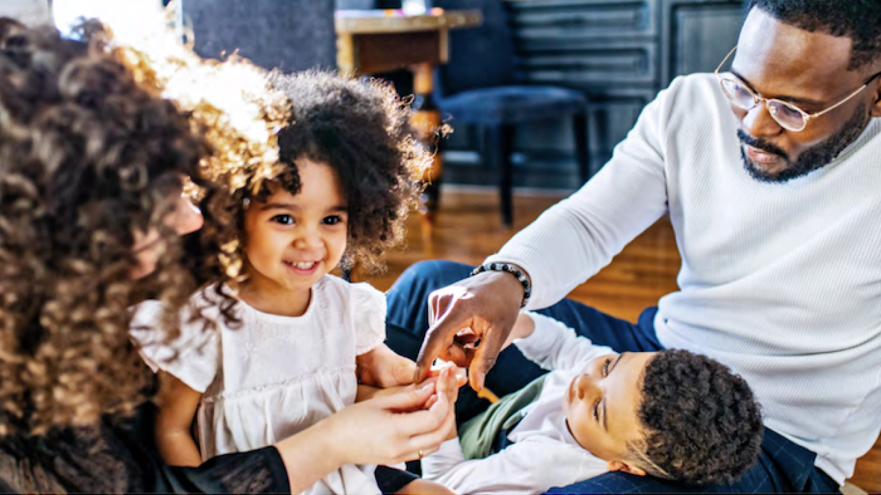 Black family of four seated on the floor of their home.