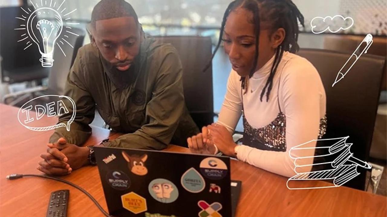 Two people sat next to each other at a table, looking at a laptop