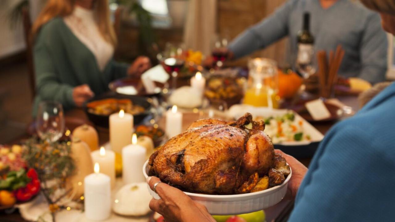 Thanksgiving dinner table with guests and a turkey are shown.