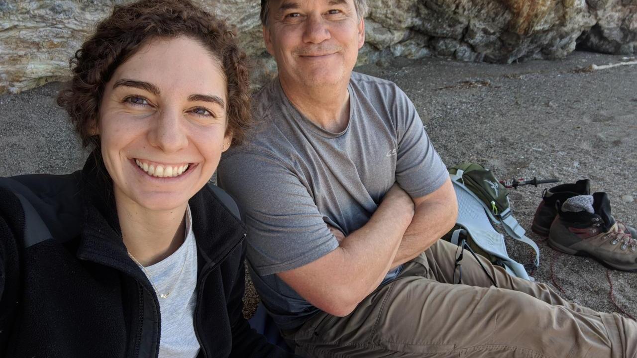 Catherine Paquette and Ned Bagno take a selfie while sitting on rocky soil. A rock wall behind them.
