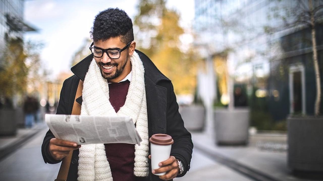 Person reading newspaper while holding coffee
