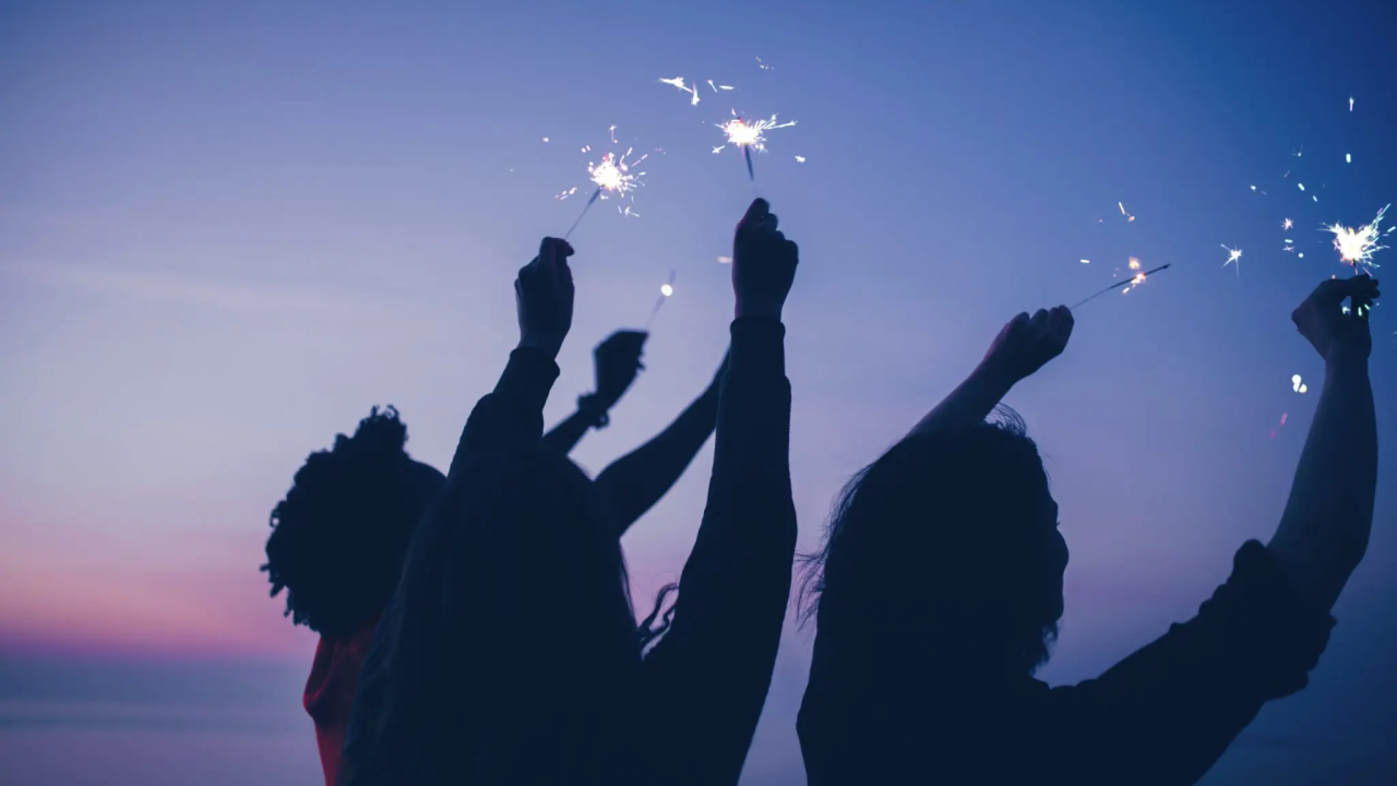 Three people waving sparklers in the dark