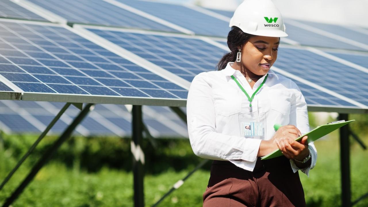 Female Wesco employee shown with a clipboard in front of a solar panel array.