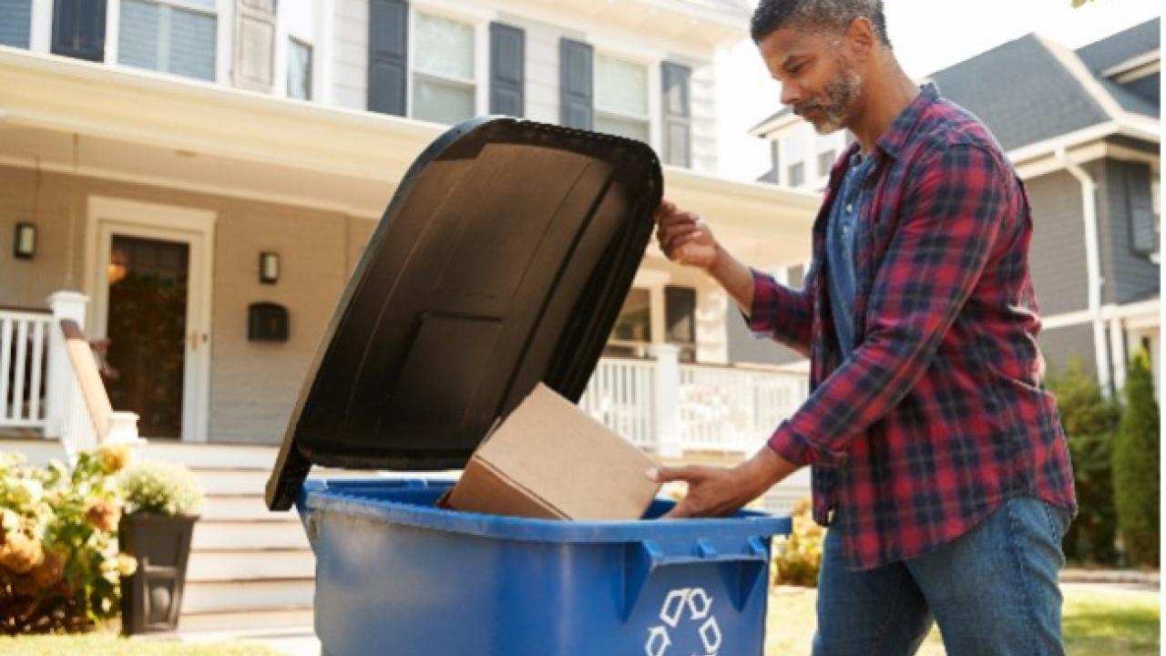 person putting box in recycling bin
