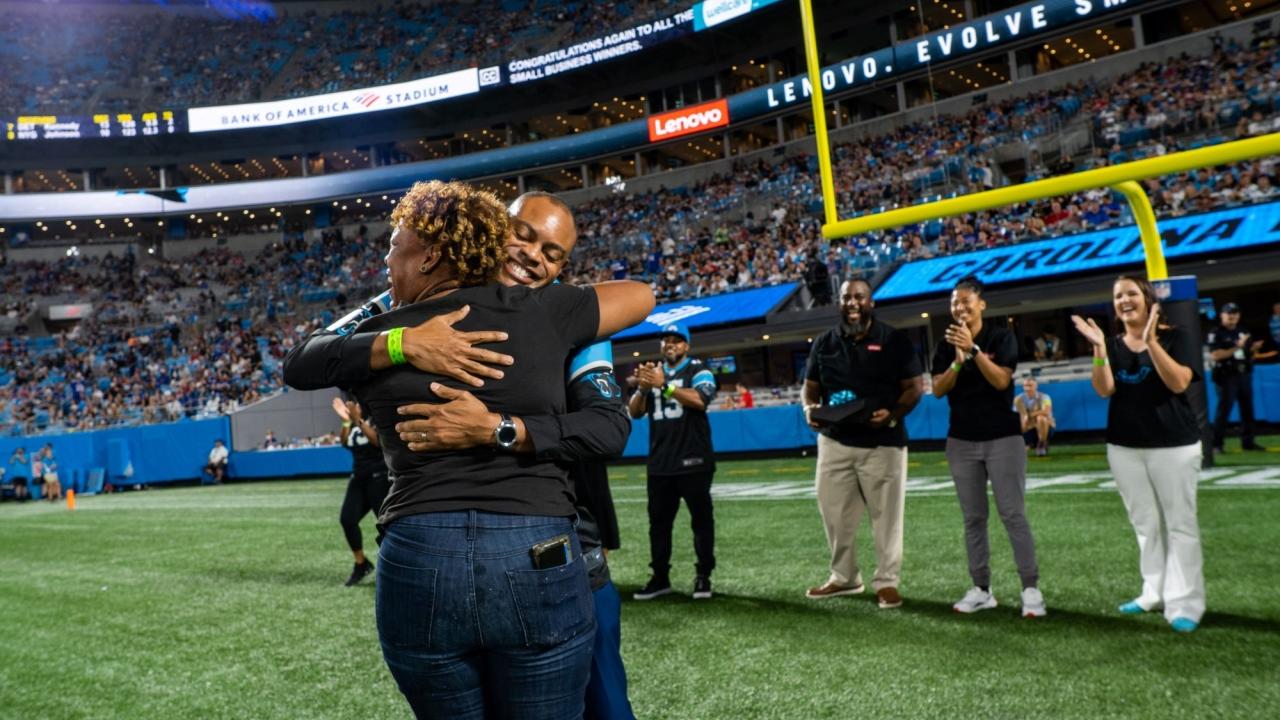 Hip Hop Smoothies of Charlotte representative hugs Lenovo North America CMO Gerald Youngblood on the Carolina Panthers field