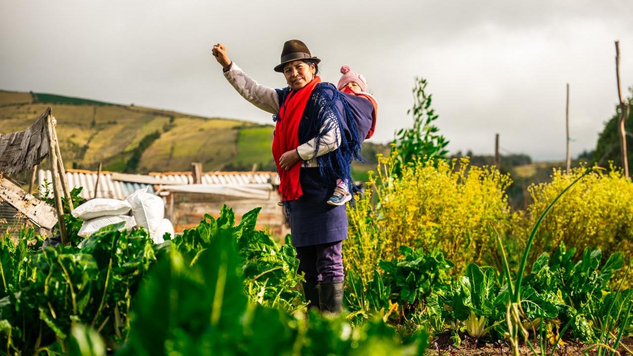 farmer stands in a field her baby strapped to her back