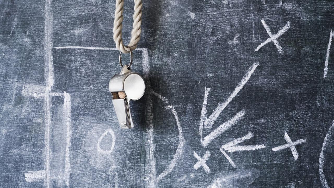 A coaches whistle hanging on a chalk board