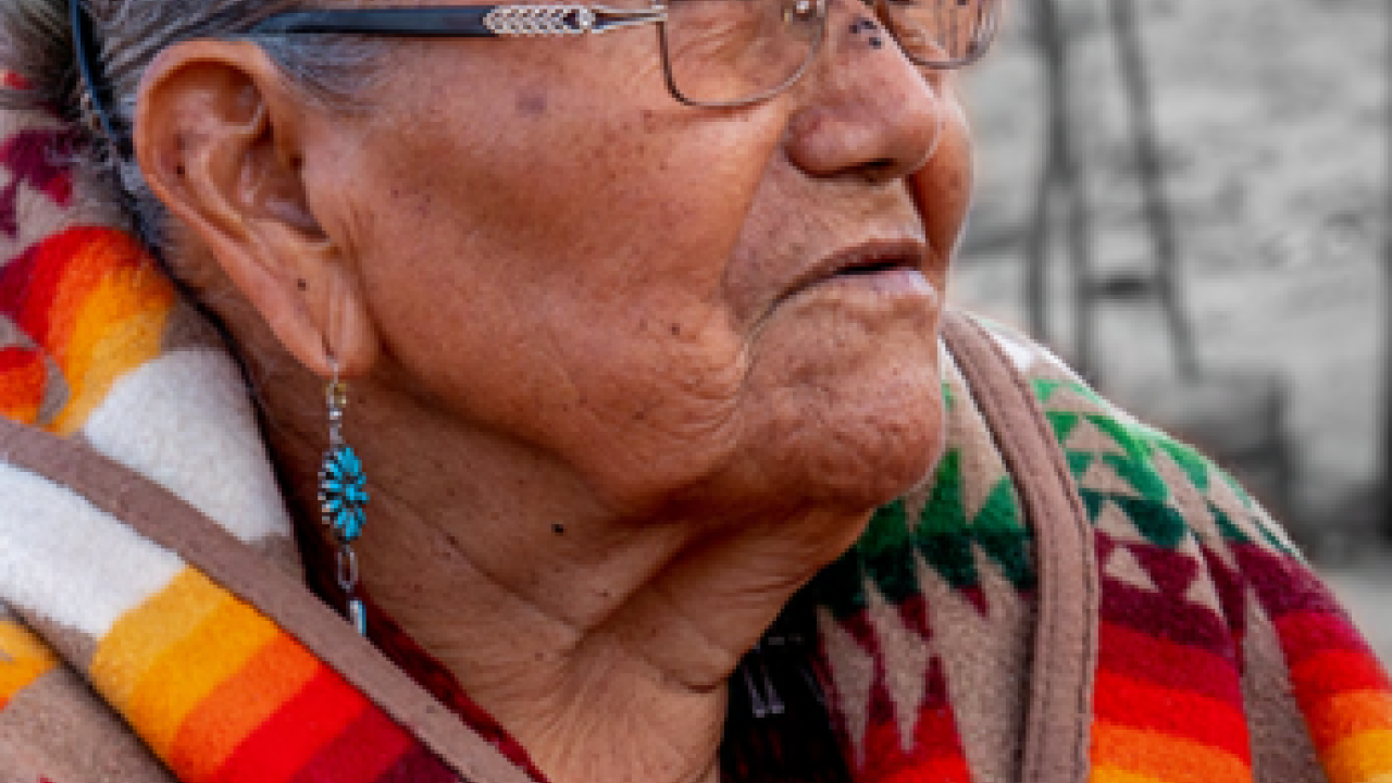 an elderly person sitting outside, a blanket wrapped around their shoulders