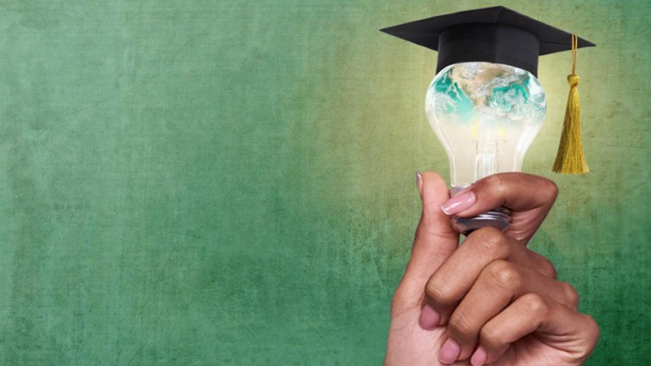 Hand holding a lightbulb with a graduate mitre on top of the bulb.