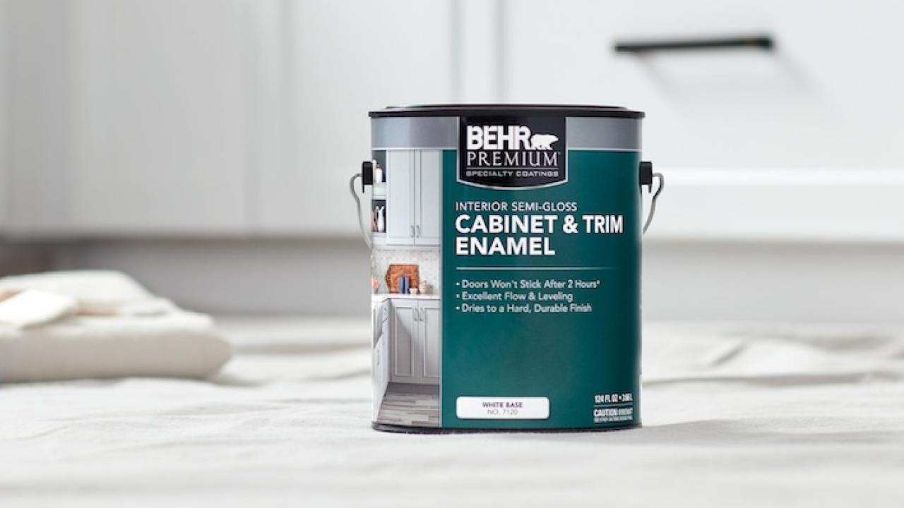A can of paint is shown on a floor on a drop cloth with other painting supplies.
