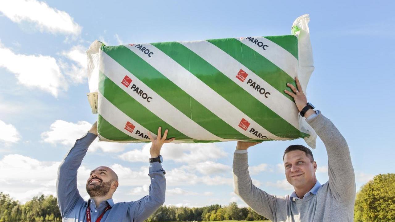 Two people holding up a bat of insulation outside