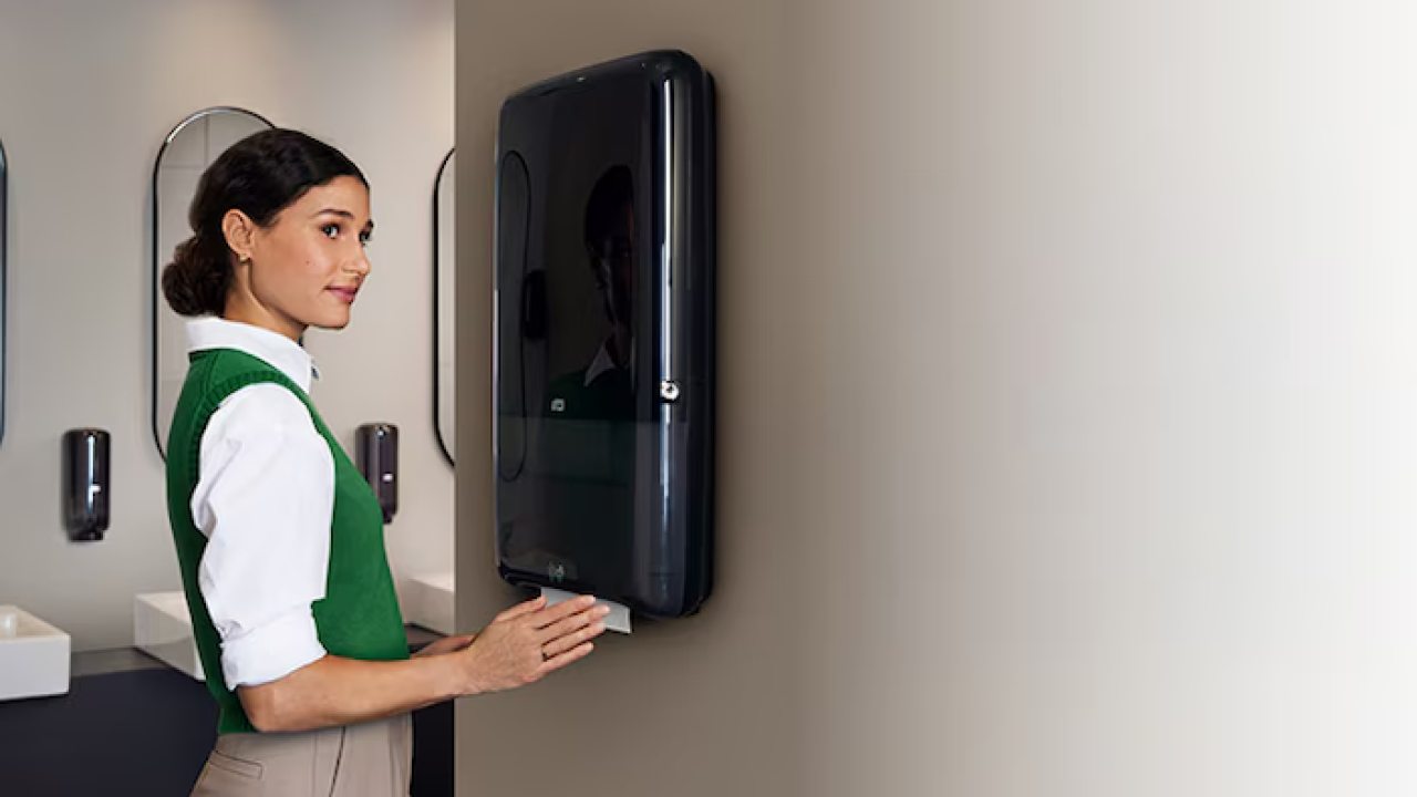 A person shown at a paper towel dispenser.